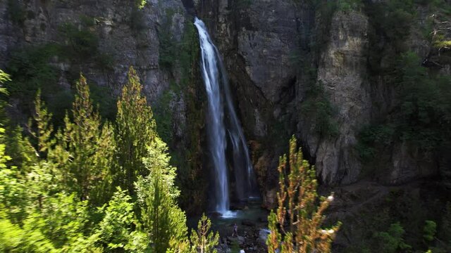 Cinematic revealing of wonderful waterfall on rocky mountain against forest trees in Teth, Albania