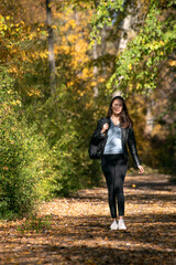 Fototapeta premium Beautiful young woman with dark hair walks along the alley of autumn park and enjoys a warm day. Lonely girl in forest