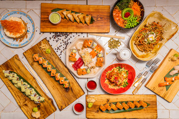 Assorted plates of Asian food and sushi on a white stoneware table. Uramaki, california roll,...
