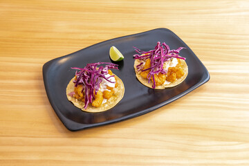 Fusion tacos with tempura fried prawns, purple cabbage, mayonnaise and lime for garnish on a black...