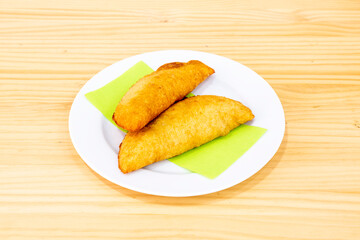 Colombian yellow corn empanadas stuffed with chicken stew with red peppers on white plate and wooden table