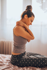 Woman suffering from back pain while sitting on bed.