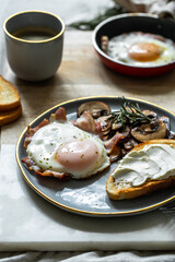 Breakfast with fried egg(sunny side up) with bacon, grilled with rosemary mushrooms and toast with cream cheese