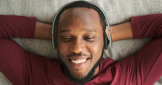 Man listening music on headphones while relaxing on bed in bedroom
