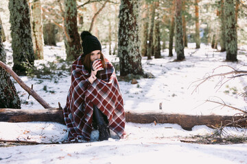 Woman sitting in winter woods and drinking coffee