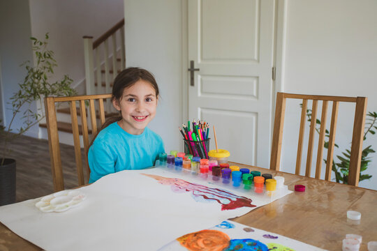 The little girl paints with paints alone at home