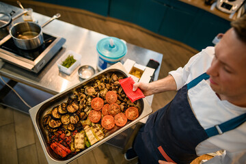 high angle view of chef with baking sheet with different baked vegetables
