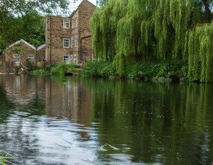 Fototapeta na wymiar Hirst Mill and the nearby willow trees reflected in the waters of the River Aire in Hirst Wood