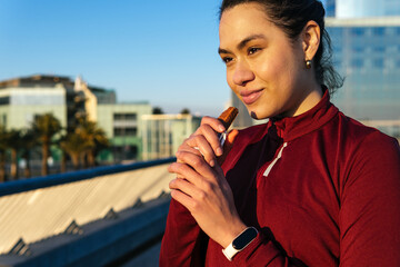 Sportswoman eating protein bar on street