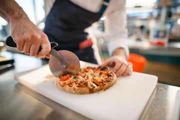 close-up of pizza on cutting board that chef cuts into pieces with cutter