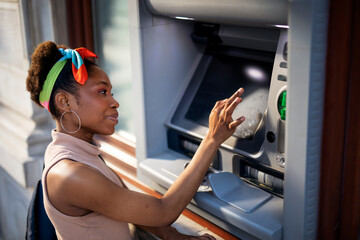 Fototapeta na wymiar Beautiful african women using ATM machine. Attractive young woman withdrawing money from credit card at ATM