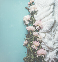 Blue background with pale pink peonies and knitted white sweater. Top view