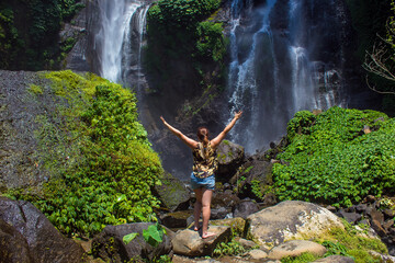 Woman posing near Sekumpul waterfalls in jungles and green rainforest on Bali island, Indonesia. Concept of freedom and success, travel and nature background