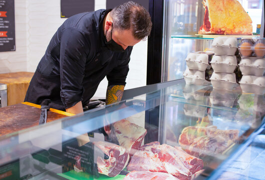 Butcher puts the meat in a refrigerated display case with farm meats