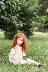 A little girl of 4 years old with long curly hair is playing outdoors in a city park. A cute child looks at the camera with a serious look.