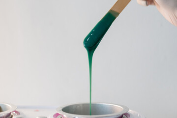 Close-up of wax heater with hot green wax and a wooden spatula