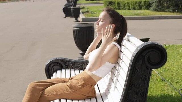 summer heat, teen girl roasts in the sun on a bench in the park