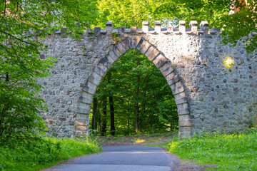 Gothic arc gate over asphalt road in the forest. Arturs Castle near Sychrov, Czech Republic