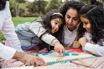 Indian parents having fun at city park playing with wood toys with their daughter and son - Main...