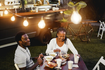 Black mother and son eating and drinking healthy food at food truck restaurant outdoor - Focus on senior woman face