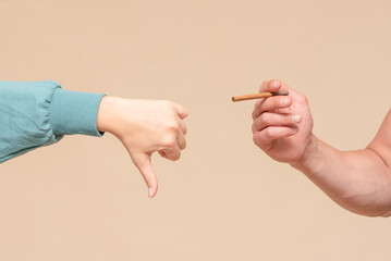 Male hand with a cigarette and woman hand which is showing a thumbs down gesture sign.