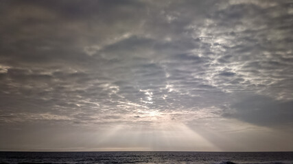 Naklejka na ściany i meble Crepuscular sun rays streaming through overcast monsoon clouds above the sea
