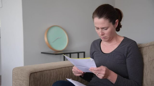 Shocked woman reading a bad letter in home living room