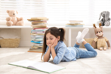 Little girl reading book on floor at home