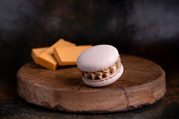 Cappuccino macaron filled with caramel cheese. On a wooden board. Rust background.
