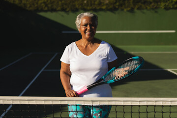 Portrait of smiling senior african american woman holding tennis racket on tennis court