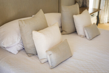 Close up of beige and white cushions and pillows on large bed in sunny bedroom