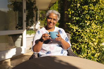 Portrait of smiling senior african american woman having tea in sunny garden - Powered by Adobe