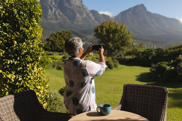 Senior african american woman taking photographs on smartphone of stunning view in sunny garden - Powered by Adobe