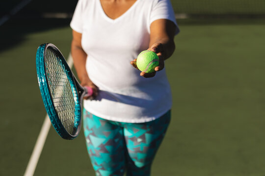 Midsection of senior african american woman holding tennis racket and ball on tennis court