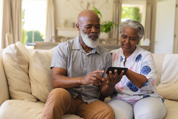 Senior african american couple sitting on sofa using smartphone