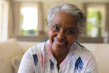Portrait of senior african american woman sitting on sofa looking at camera and smiling - Powered by Adobe