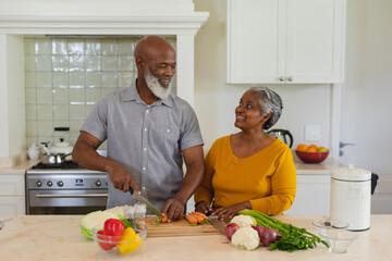 Senior african american couple cooking together in kitchen smiling