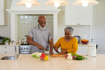 Senior african american couple cooking together in kitchen smiling