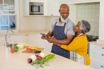 Senior african american couple cooking together in kitchen using tablet