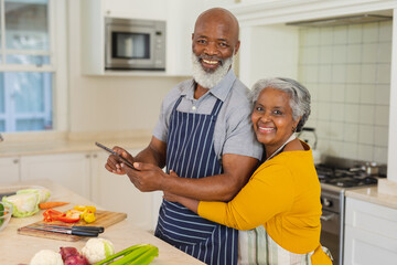 Portrait of senior african american couple cooking together in kitchen using tablet