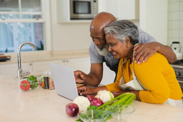 Senior african american couple cooking together in kitchen using laptop