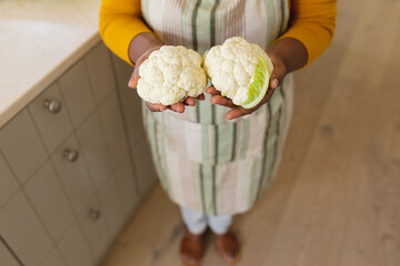 Mid section view of senior african american woman holding cauliflowers in kitchen - Powered by Adobe