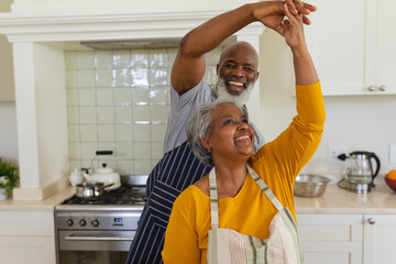 Senior african american couple dancing together in kitchen smiling
