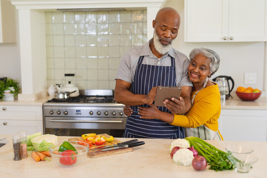 Senior african american couple cooking together in kitchen using tablet