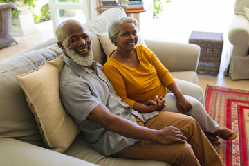 Portrait of senior african american couple sitting on sofa holding hands looking at camera smiling