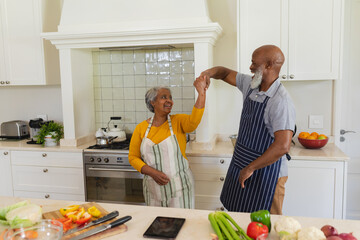 Senior african american couple dancing together in kitchen smiling
