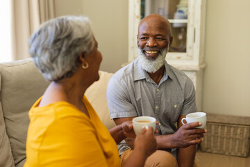 Senior african american couple sitting on sofa drinking coffee in living room