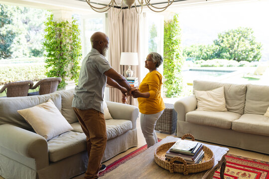 Senior african american couple dancing together in living room smiling