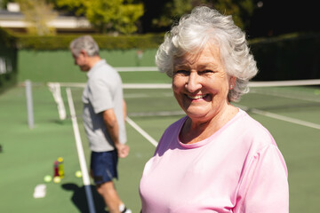 Portrait of senior caucasian woman looking at camera and smiling on tennis court