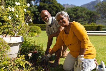 Portrait of senior african american couple spending time in sunny garden together planting flowers